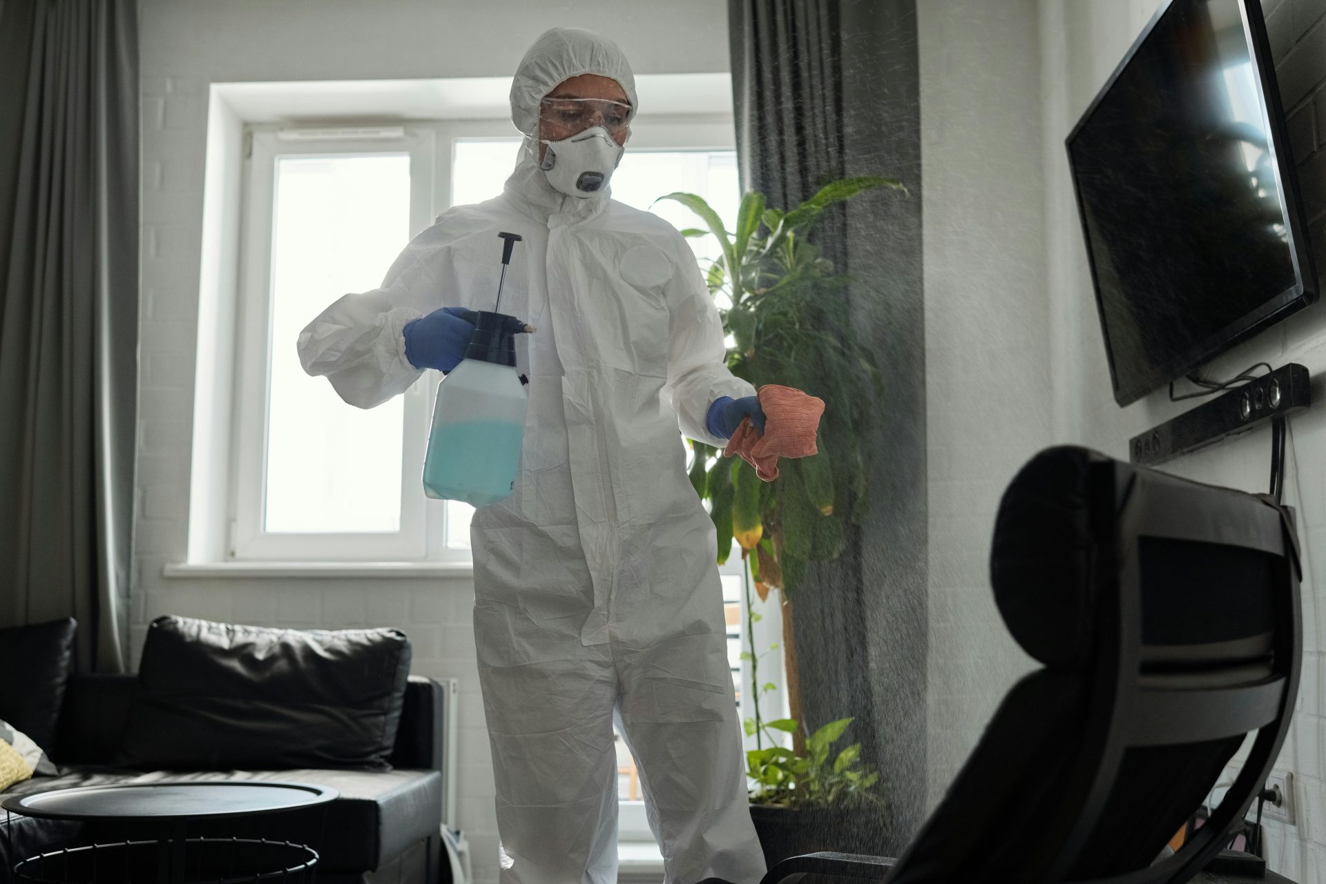 Ein professioneller Reinigungskraft in Schutzkleidung desinfiziert einen Innenbereich mit einer Sprühflasche und einem Tuch.